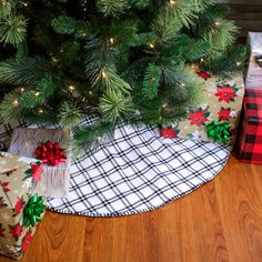 a christmas tree with presents under it on the floor next to a plaid blanket and wrapped present boxes