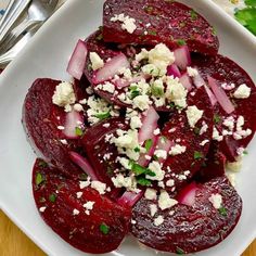 a white plate topped with beets and feta cheese on top of a wooden table