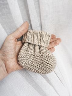 a person holding a knitted baby booties in their hands with the text first baby booties knitting pattern by woollure