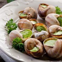 some snails are on a white plate with green sauce and parsley in the middle