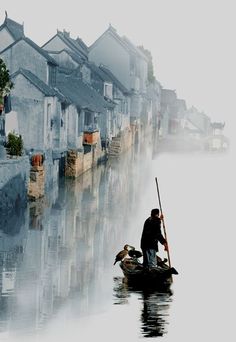 a man on a small boat in the middle of a river with houses behind him