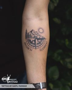 a man's arm with a compass tattoo on it and mountains in the background