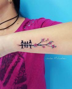 a woman's arm with three birds sitting on a tree branch and pink flowers