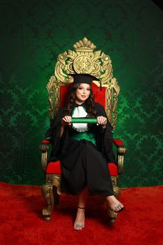 a woman sitting on top of a red chair in front of a green and gold wall