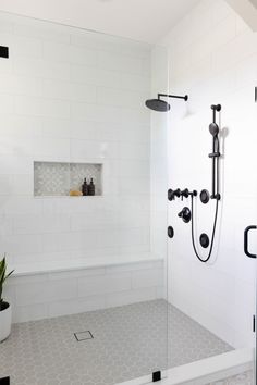 a white tiled bathroom with black fixtures and shower head mounted on the wall above the bathtub