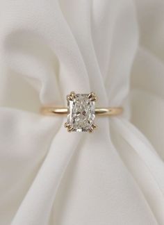 an engagement ring with a cushion cut diamond in the center on a white satin background