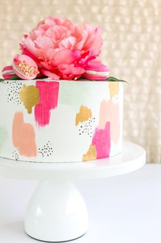 a white cake with pink flowers on top and gold foiling around the edges, sitting on a pedestal