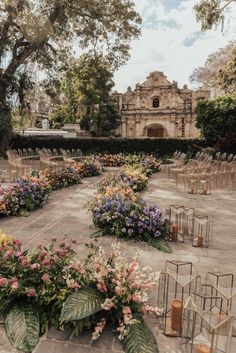 an outdoor ceremony set up with chairs and flowers in the foreground, surrounded by greenery