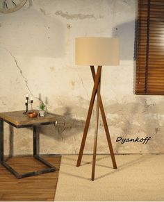 a wooden floor lamp next to a table with a clock on the wall behind it