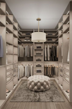 a walk - in closet with an ottoman and several clothes on hangers next to it