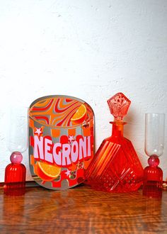 an orange and red bottle sitting on top of a wooden table next to two empty glasses