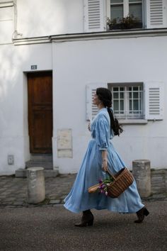 a woman in a blue dress is walking down the street with a basket and flowers