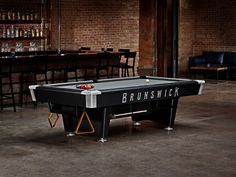 a pool table in the middle of a room with bar stools and tables behind it