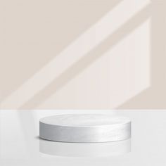 a round white table with a shadow on the wall behind it and a light colored background