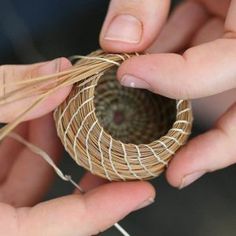 two hands are holding twine that is wrapped around a round object with yarn on it