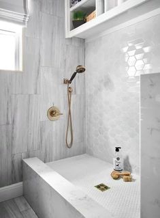 a bathroom with white hexagonal tiles and gold fixtures on the shower wall, along with a brass faucet