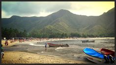 several boats on the beach with mountains in the background and people walking along the shore