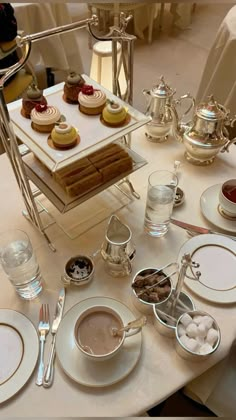 a table topped with plates and cups filled with desserts next to silverware on top of a white table cloth