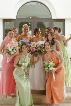 a group of women standing next to each other in front of a building holding bouquets