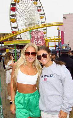 two women standing next to each other in front of a ferris wheel at an amusement park