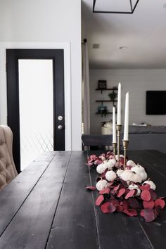 a dining room table with candles and flowers on the top, in front of a black door