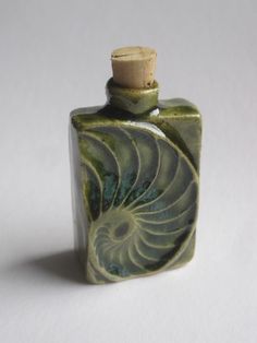 a green and white bottle with a cork top sitting on a table in front of a white background