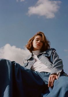 a woman sitting on the ground with her legs crossed and looking off into the distance