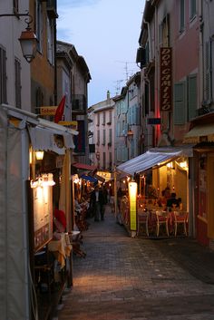 an alley way with people sitting at tables and eating food on the side walk in front of buildings