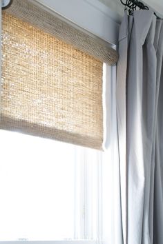 an open window with white curtains and light coming through the top blinds, in front of a curtain rod