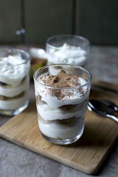 two glasses filled with dessert sitting on top of a wooden cutting board