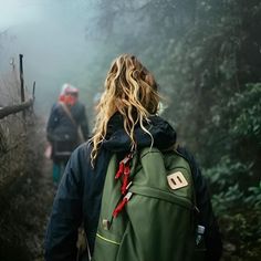 two people walking in the woods on a foggy day with backpacks over their shoulders