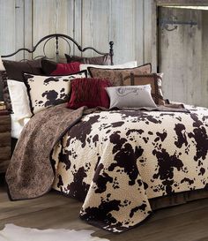 a cow print comforter set on a bed in a room with wooden walls and flooring