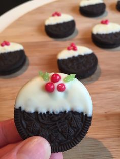 a hand holding an oreo cookie with white frosting and red berries