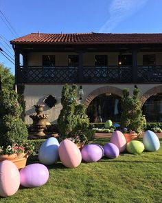 some fake eggs are lined up in front of a house with flowers and bushes on the lawn