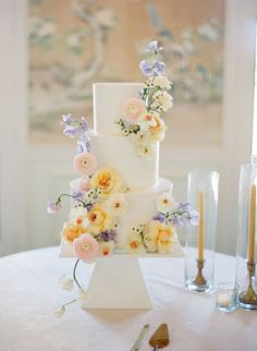 a three tiered cake with flowers on it sitting on top of a table next to candles