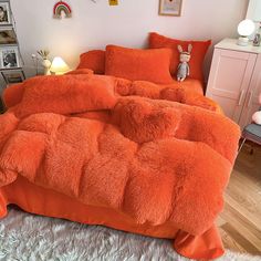 an orange bed with fluffy pillows on it and a stuffed animal sitting in the corner