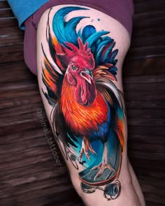 a colorful rooster tattoo on the thigh