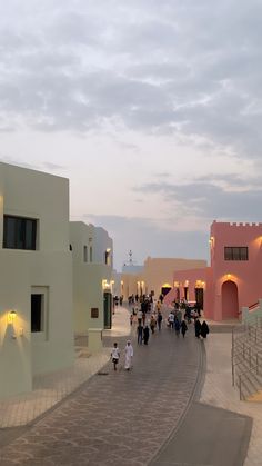 many people are walking down the street in front of some pink and white buildings at dusk