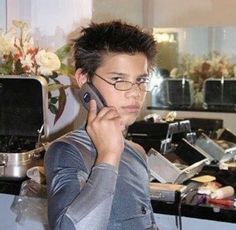 a young man wearing glasses is talking on his cell phone while standing in the kitchen