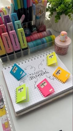 a notebook with sticky notes and pens on it sitting next to a potted plant