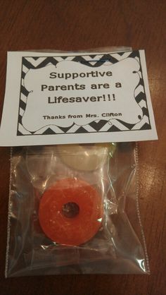 a donut wrapped in plastic on top of a wooden table next to a sign that says, support parents are a lifesaver