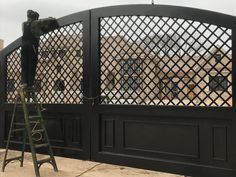 a man standing on top of a ladder next to a black gate with an iron fence