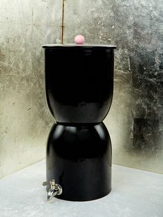 a black toilet sitting on top of a white floor next to a metal tank with a pink ball in it