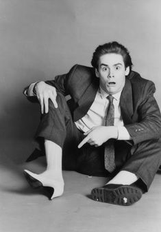 a black and white photo of a man in a suit sitting on the floor with his legs crossed