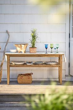 a wooden table sitting on top of a porch next to a white building with glass vases