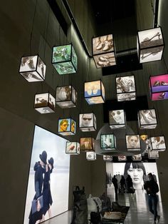 people are walking through an art gallery with many pictures hanging from the ceiling and on the walls