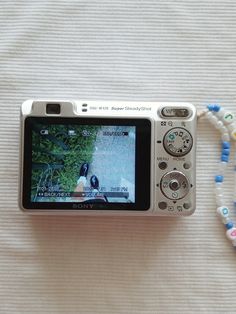 a white camera sitting on top of a bed next to a beaded necklace