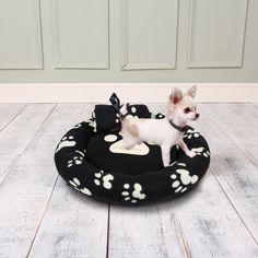 a small white dog standing on top of a black and white bed with paw prints