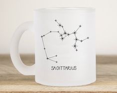 the zodiac sign sagittarius on a white coffee mug sitting on a wooden table