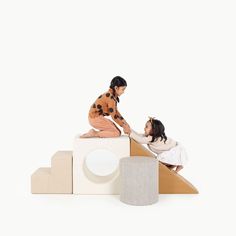 two children are playing on a cardboard structure with an adult holding the child's hand